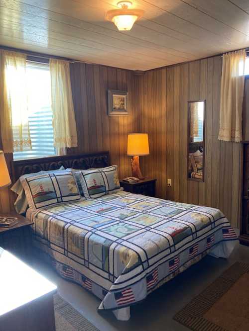 Cozy bedroom with wooden walls, a patterned quilt on the bed, and warm lighting from lamps.