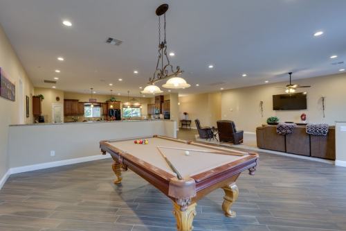 A spacious game room featuring a pool table, modern lighting, and an open kitchen area in the background.