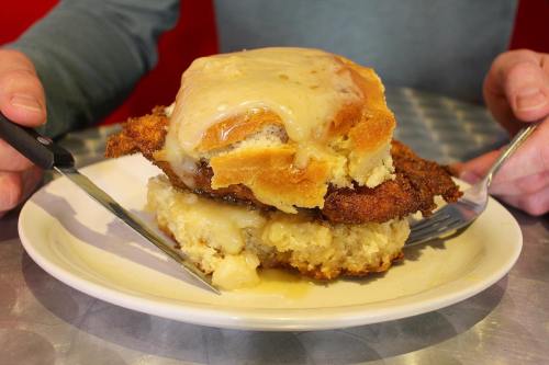 A person holds a plate with a large chicken and biscuit dish topped with creamy gravy.