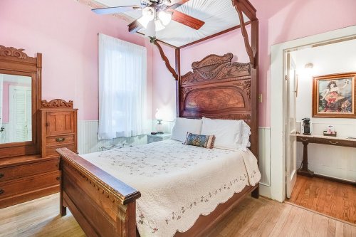 Cozy bedroom with a wooden four-poster bed, pink walls, and a vintage dresser, featuring soft lighting and a warm atmosphere.