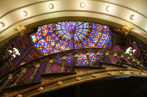 A spiral staircase with ornate railings, leading up to a colorful stained glass dome.
