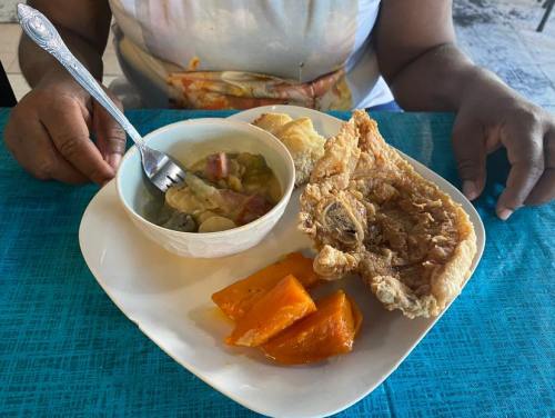 A plate of food featuring fried meat, sweet potatoes, and a bowl of soup, with a person holding a spoon.