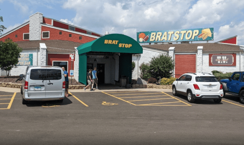 Exterior of Brat Stop restaurant with a green awning, cars parked outside, and people entering on a sunny day.