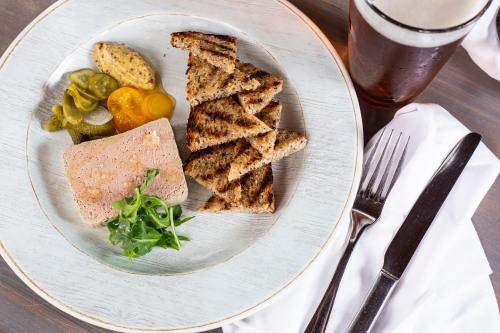 A plate with sliced pâté, toasted bread, pickles, mustard, and a glass of beer on a wooden table.