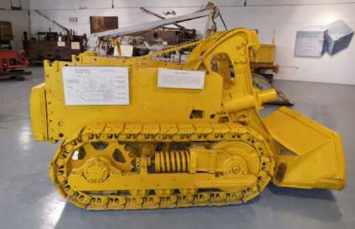 A vintage yellow bulldozer displayed in a museum, showcasing its tracks and front blade.