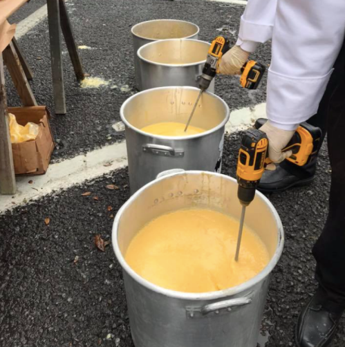 Four large pots of yellow mixture, each with a drill mixer, set on a pavement.