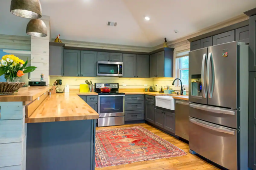 Modern kitchen with gray cabinets, stainless steel appliances, a wooden countertop, and a colorful rug. Bright and inviting space.