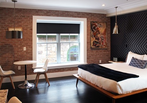 Modern hotel room featuring a bed, small dining table, and large window with brick and wood accents.