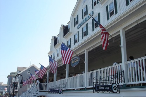 A historic building with American flags hanging from the porch, featuring signs for a restaurant and a photo dog area.