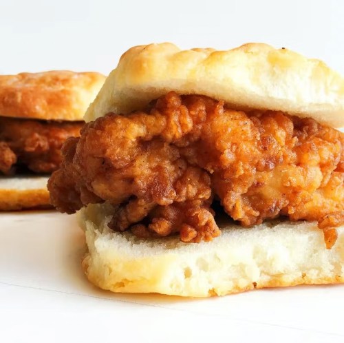 A close-up of a crispy fried chicken sandwich served on a fluffy biscuit.