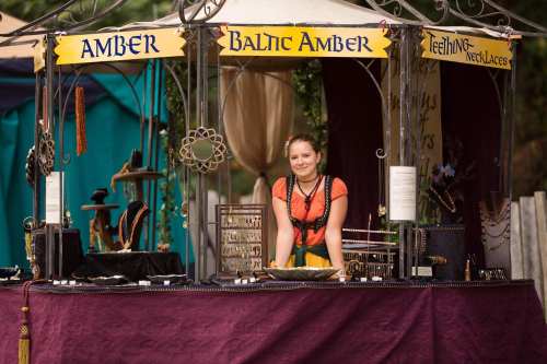 A vendor at a market stall displays amber jewelry, smiling and wearing a colorful outfit.