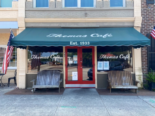 A quaint café with a green awning, wooden benches, and a welcoming entrance, established in 1933.