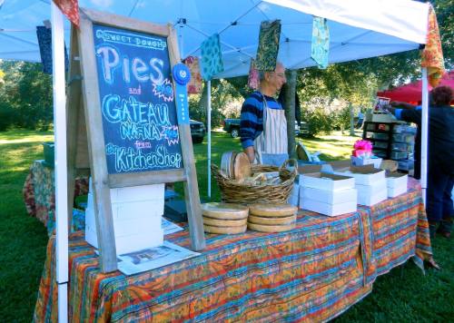 A vendor at a market stand displays pies and baked goods, with colorful decorations and a sign reading "Sweet Dough."