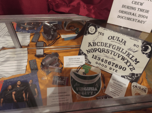 Display case featuring a Ouija board, cameras, and memorabilia from a 2004 documentary about ghost hunting.