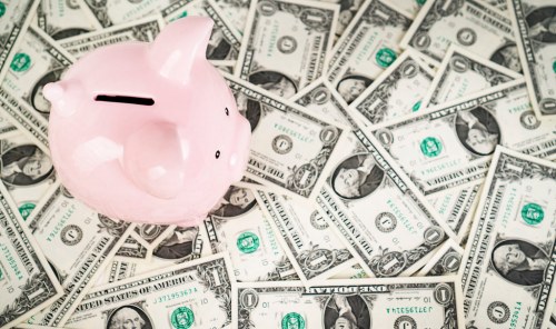 A pink piggy bank sits on a spread of one-dollar bills, symbolizing saving and finance.
