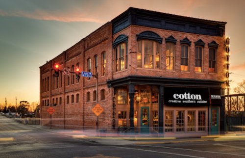 Historic brick building at sunset, featuring a restaurant named "cotton" with large windows and street signs nearby.