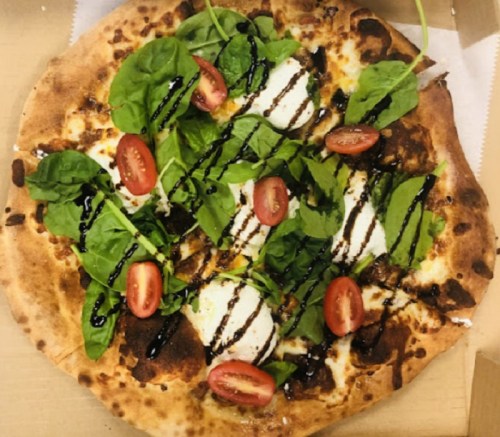 A pizza topped with fresh spinach, cherry tomatoes, and drizzled balsamic glaze on a crispy crust.