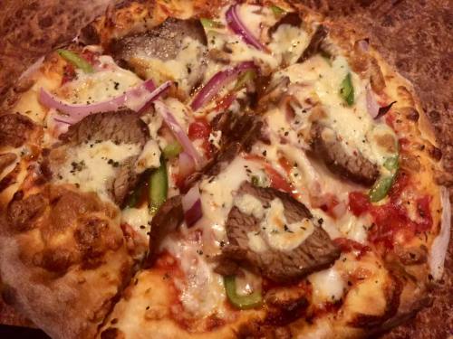 A close-up of a pizza topped with cheese, sliced beef, red onions, and green peppers on a golden crust.