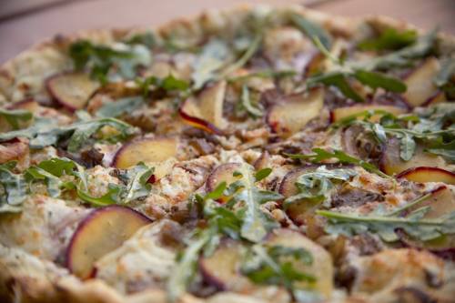 A close-up of a pizza topped with arugula, sliced potatoes, and cheese on a golden crust.