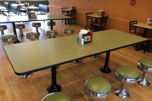 A spacious diner interior featuring a long table with green stools and condiment holders on the table.