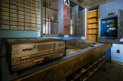 An old, dusty control panel with buttons and dials, set in a vintage room with shelves and a bulletin board.