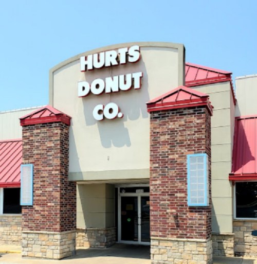 Exterior of Hurts Donut Co. building with a brick facade and red roof under a clear blue sky.