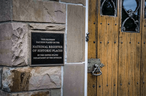Plaque on a stone wall next to a wooden door, indicating the property is on the National Register of Historic Places.
