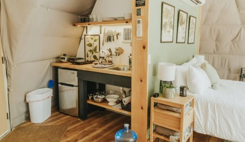 Cozy interior of a glamping tent featuring a kitchenette, dining area, and a bed with soft linens.