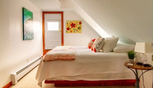 Cozy bedroom with a sloped ceiling, a bed with decorative pillows, and a small table beside it. Bright and inviting decor.