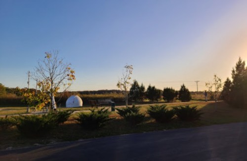 A serene landscape with trees, a white dome structure, and a clear sky at sunset.