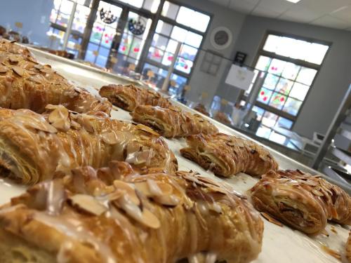A close-up of freshly baked almond pastries drizzled with icing, displayed in a bright bakery setting.