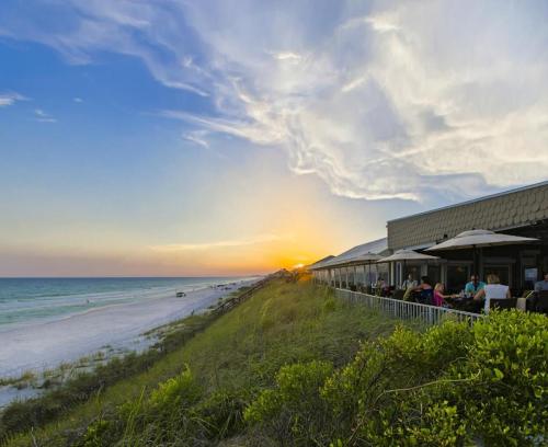 A beachside restaurant at sunset, with diners enjoying the view and waves lapping at the shore.
