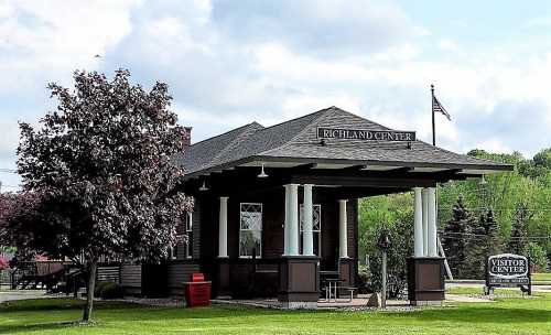 Historic visitor center building with a sign reading "Richland Center," surrounded by greenery and a flag.