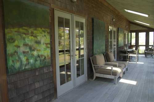 A porch with two large paintings, comfortable seating, and wooden walls, surrounded by greenery.