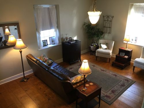 Cozy living room with a brown sofa, lamps, a rug, and natural light from windows.