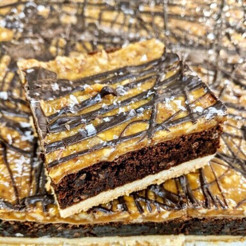 A close-up of a layered dessert featuring chocolate brownie, peanut butter, and a drizzle of chocolate with sea salt.