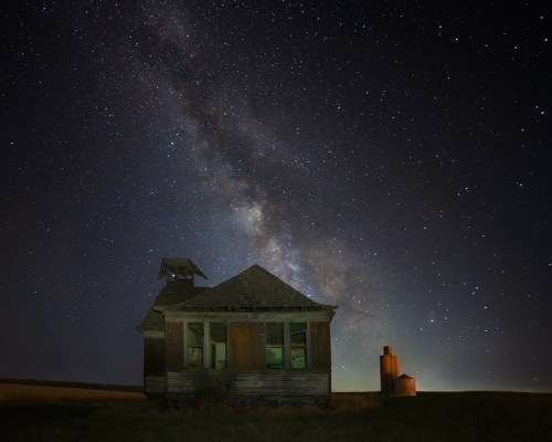 A dilapidated house and silo under a starry sky, with the Milky Way visible in the background.