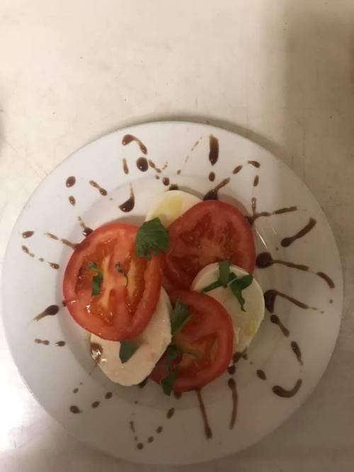 A plate of sliced tomatoes and mozzarella cheese drizzled with balsamic glaze and garnished with fresh herbs.