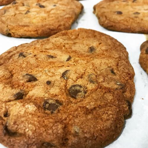 Close-up of freshly baked chocolate chip cookies on parchment paper, golden brown with chocolate chunks visible.