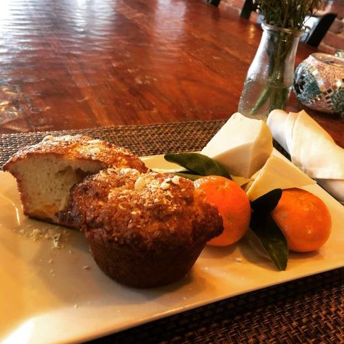 A plate with a muffin, a slice of cake, two oranges, and pieces of cheese, set on a wooden table.