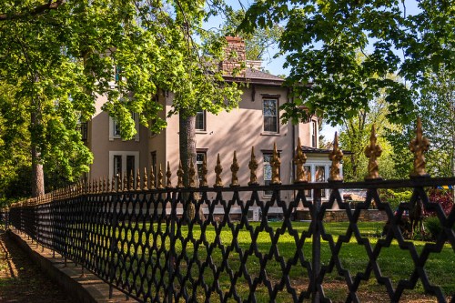 A charming house surrounded by lush greenery and a decorative black fence with gold accents.