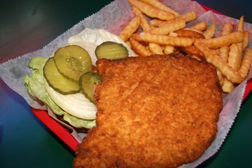 A plate with a crispy fried chicken breast, lettuce, pickles, and crinkle-cut fries in a red basket.