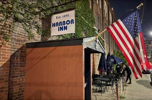 Exterior of Harbor Inn, established 1895, featuring a large American flag and outdoor seating at night.