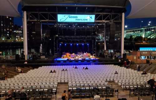 An empty outdoor concert venue at night, featuring a stage with blue lights and rows of empty seats.