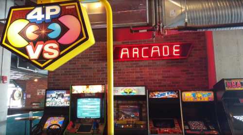 Colorful arcade sign with "4P VS" and "ARCADE" illuminated, featuring classic arcade game machines in a vibrant setting.