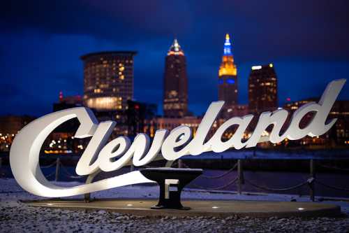 Cleveland sign illuminated at night with city skyline in the background.