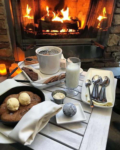 A cozy scene with warm cookies, ice cream, chocolate, and a glass of milk by a crackling fireplace.