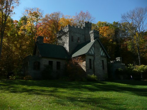 A stone castle surrounded by colorful autumn trees and a green lawn under a clear blue sky.