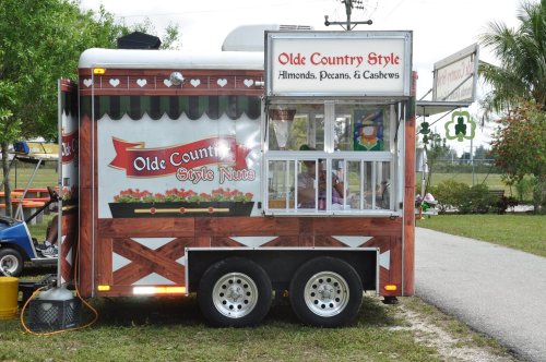 A food truck with a wooden design, featuring a sign for "Olde Country Style Nuts" selling almonds, pecans, and cashews.