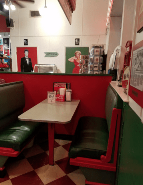 A retro diner booth with green seats, a table, and vintage decor featuring iconic figures on the walls.